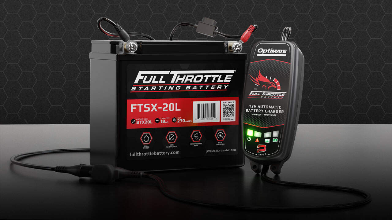 A Full Throttle FTSX-20L starting battery is connected to an OptiMate 12V automatic battery charger on a black surface with a hexagonal pattern background.