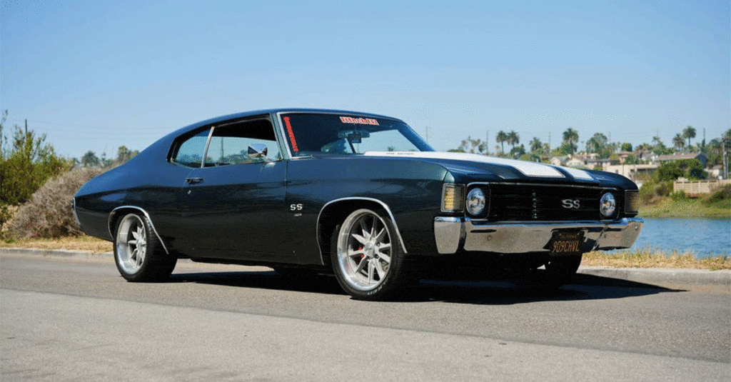 A black chevrolet chevelle ss parked by a roadside with a water body and palm trees in the background.
