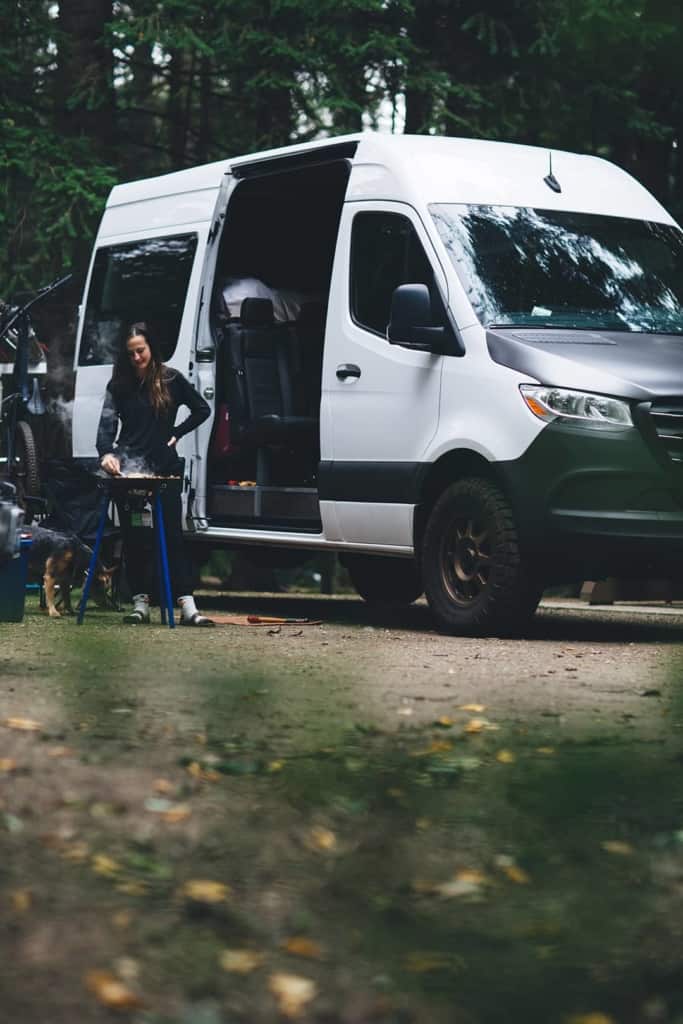 Cameron's companions camping in his van and preparing a meal in the woods.