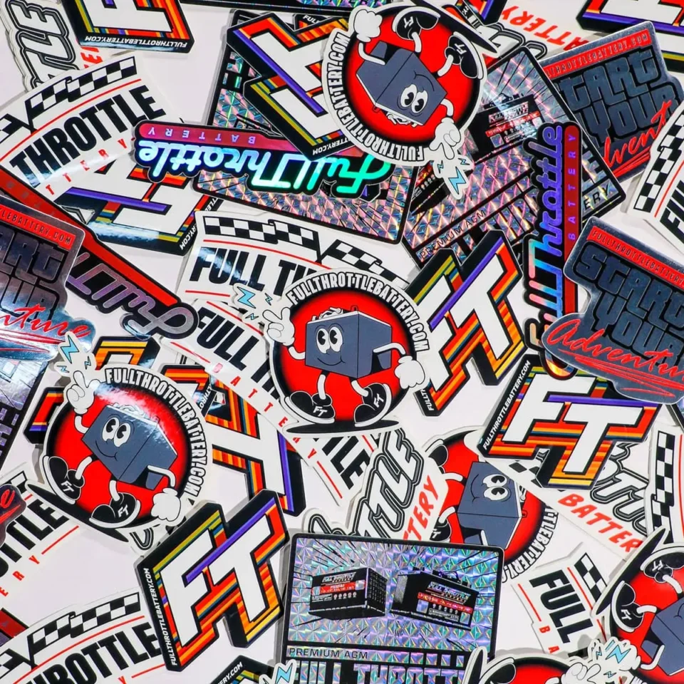 An assortment of colorful Full Throttle Battery stickers featuring various designs, logos, and a cartoon character. The stickers have bold text and vibrant graphics.