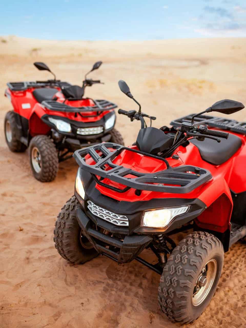 Two red all-terrain vehicles (ATVs) parked on sandy terrain under a clear sky.