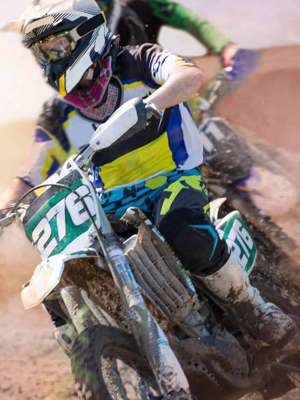 A person wearing a helmet rides a dirt bike with the number 276, kicking up dust on a dirt track, while another rider follows closely.