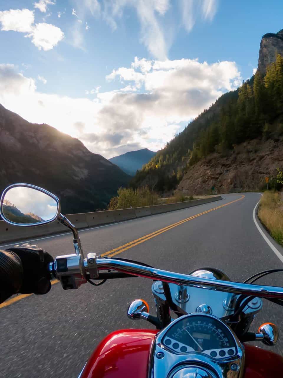 Motorcycle ride on a winding mountain road with trees and a cloudy sky in the distance.