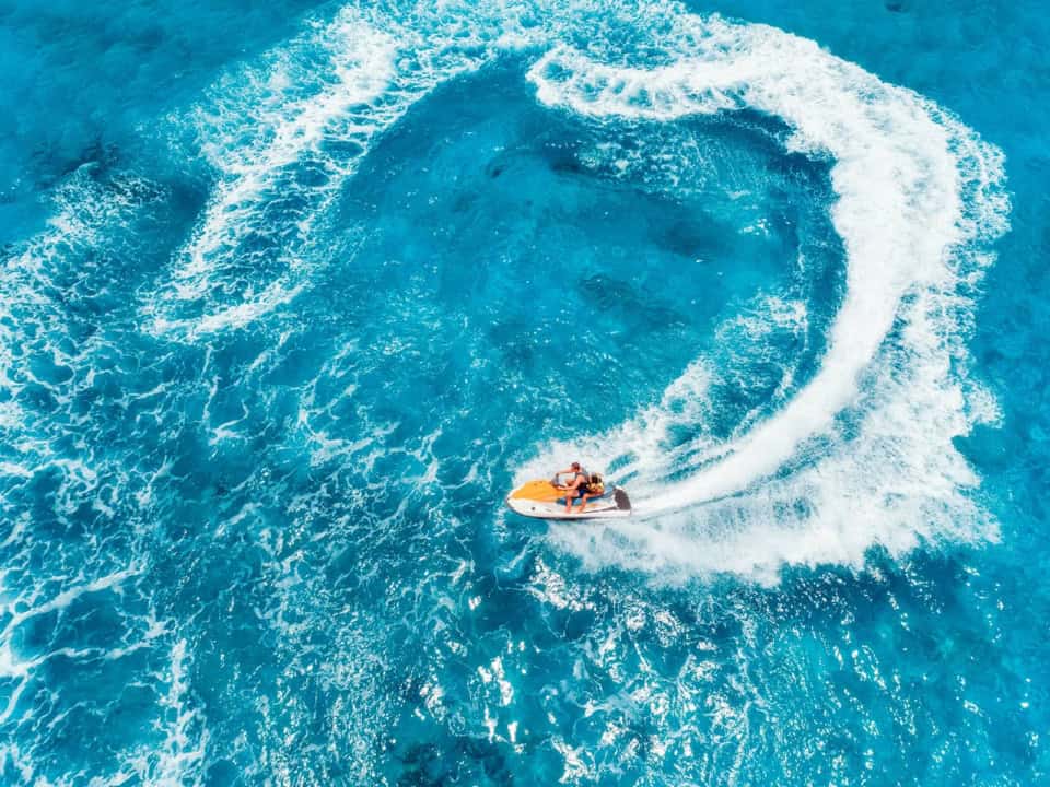 Person riding a jet ski on clear blue water, creating a circular wake pattern.