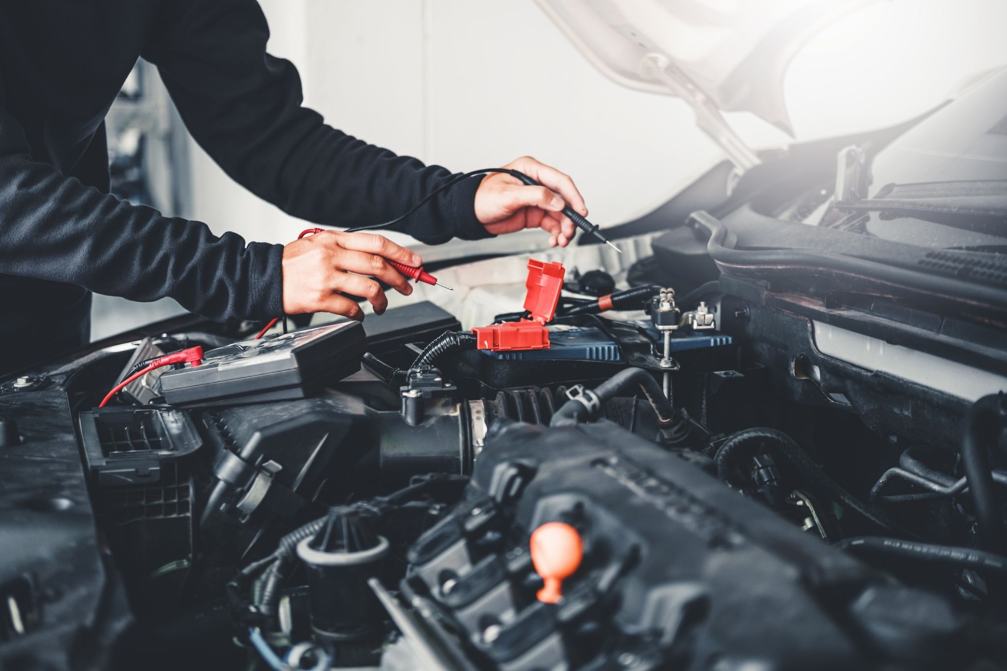 Person using a multimeter to check a car battery under the hood of a vehicle.