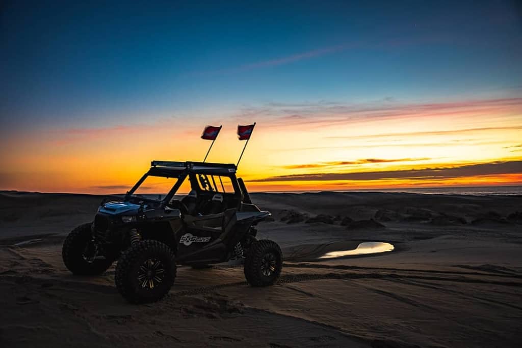 A UTV perched upon a small dune as the sunset hides behind clouds.